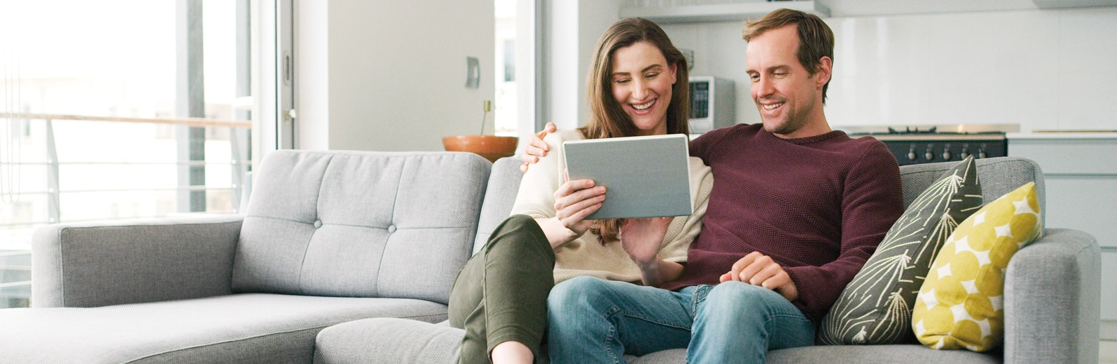 couple-on-the-couch-looking-at-tablet-1600x522.webp