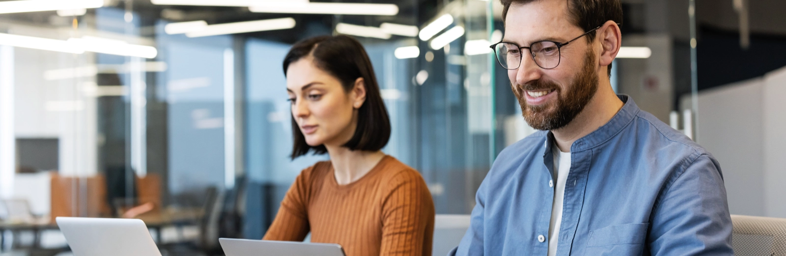 man-and-woman-working-in-office-on-laptops-1600x522.webp